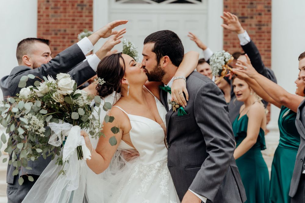 Bride and groom kissing underneath the bridal party's outstretched arms.