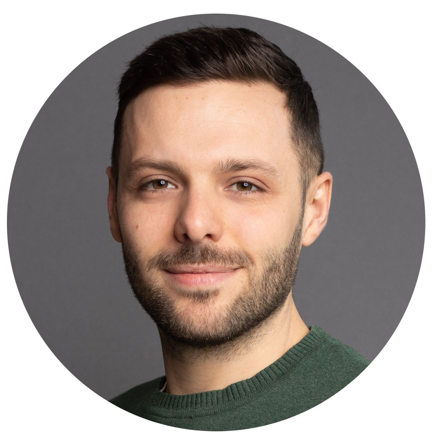Professional headshot of someone in a dark green sweater with short dark hair and facial hair against a grey background.