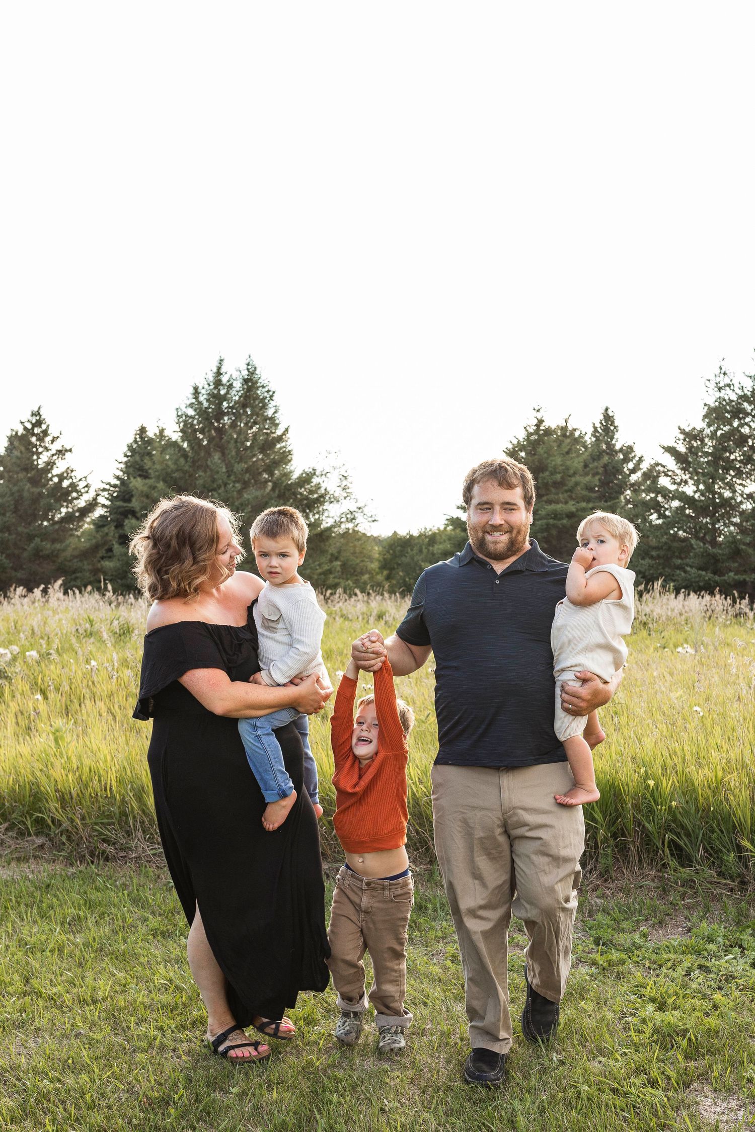 A mother and a father each holding a child while swinging a third child between them with a Central Minnesotan backdrop