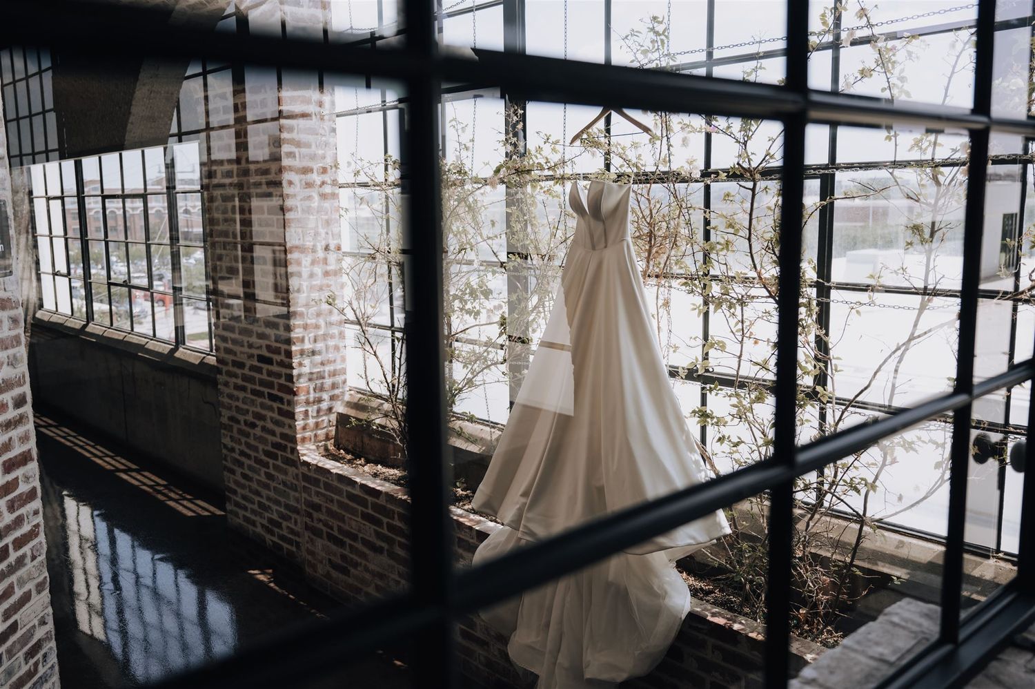 An elegant white wedding dress hanging in an industrial brick and glass space.