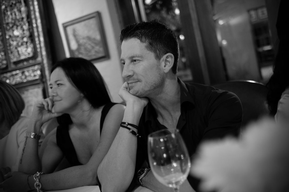 Black and white photo of a man and woman sitting together at a wedding reception table with wine.