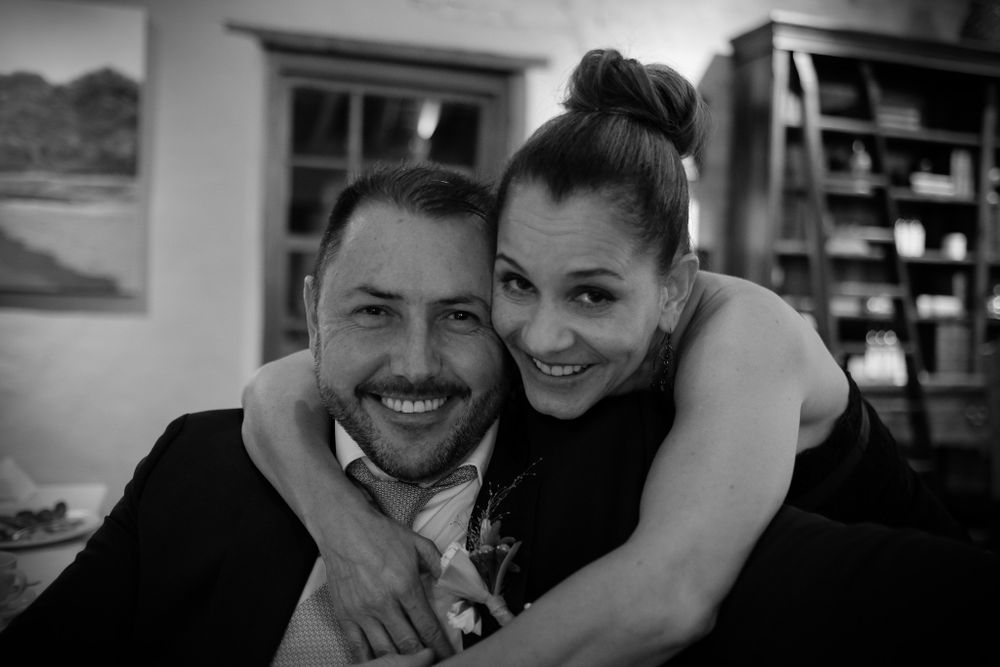 Black and white photo of a laughing couple hugging closely together at an indoor wedding reception.