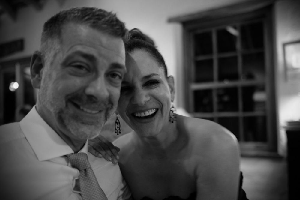 Black and white selfie of a smiling couple laughing together at a joyful wedding reception.