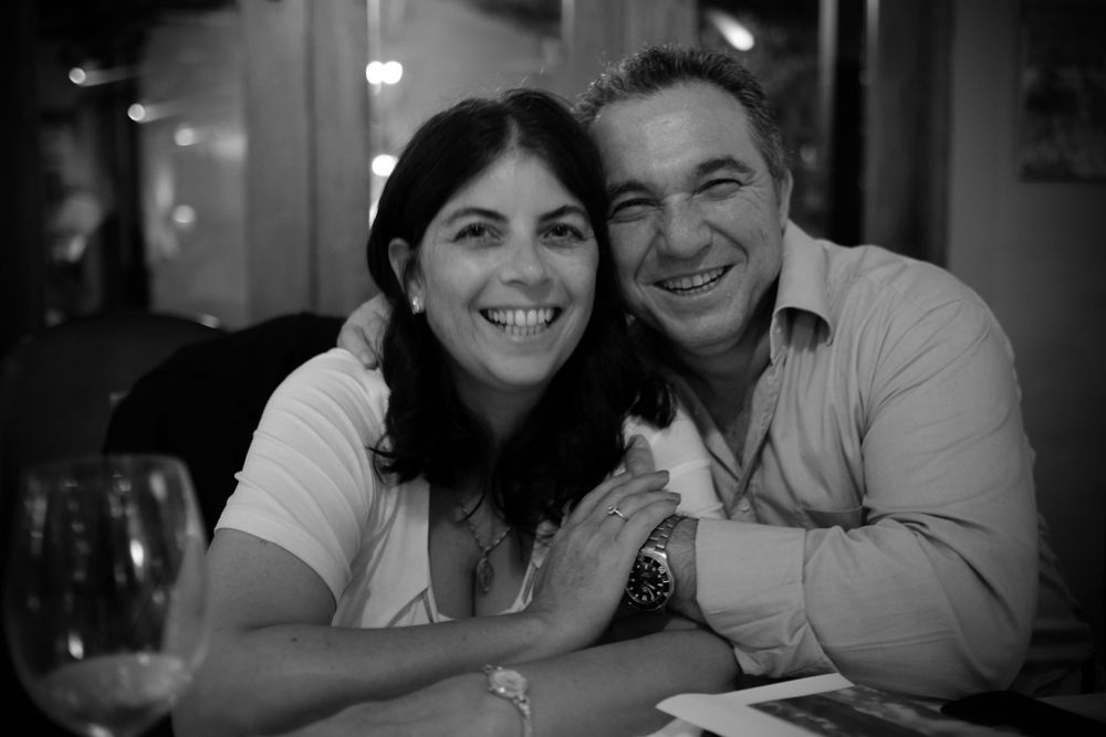 Happy couple smiling and posing together at a restaurant table in black and white photo.