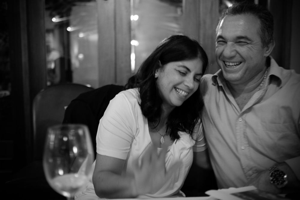 Laughing couple sharing a joyful moment at a dinner table with a wine glass nearby.