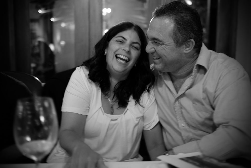 Joyful couple sharing a laugh at a dinner table with a wine glass beside them.