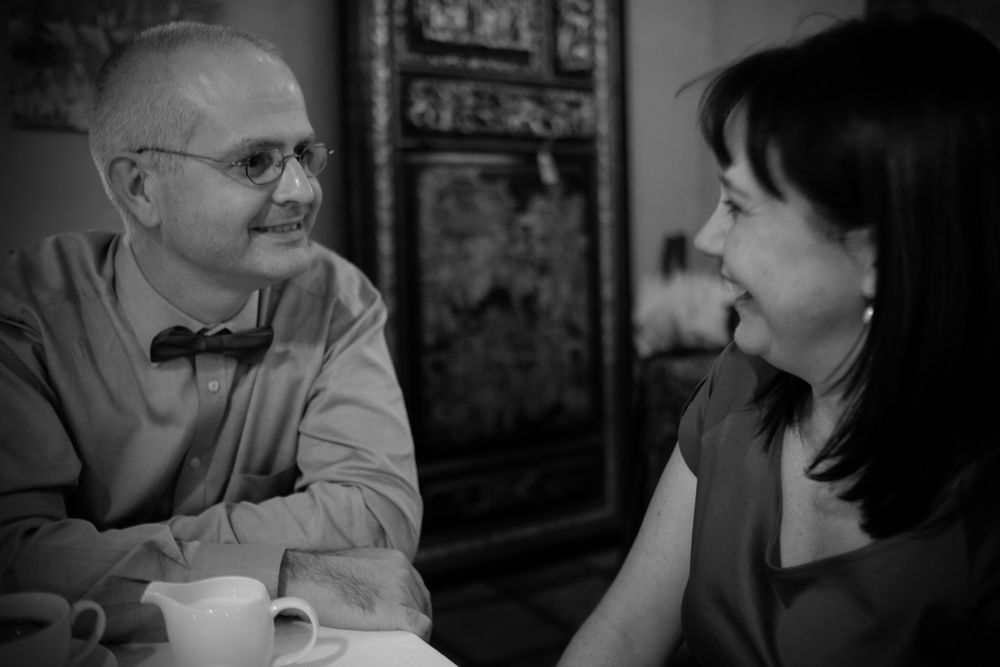 Mature couple smiling and talking intimately over coffee at a table with ornate decor.