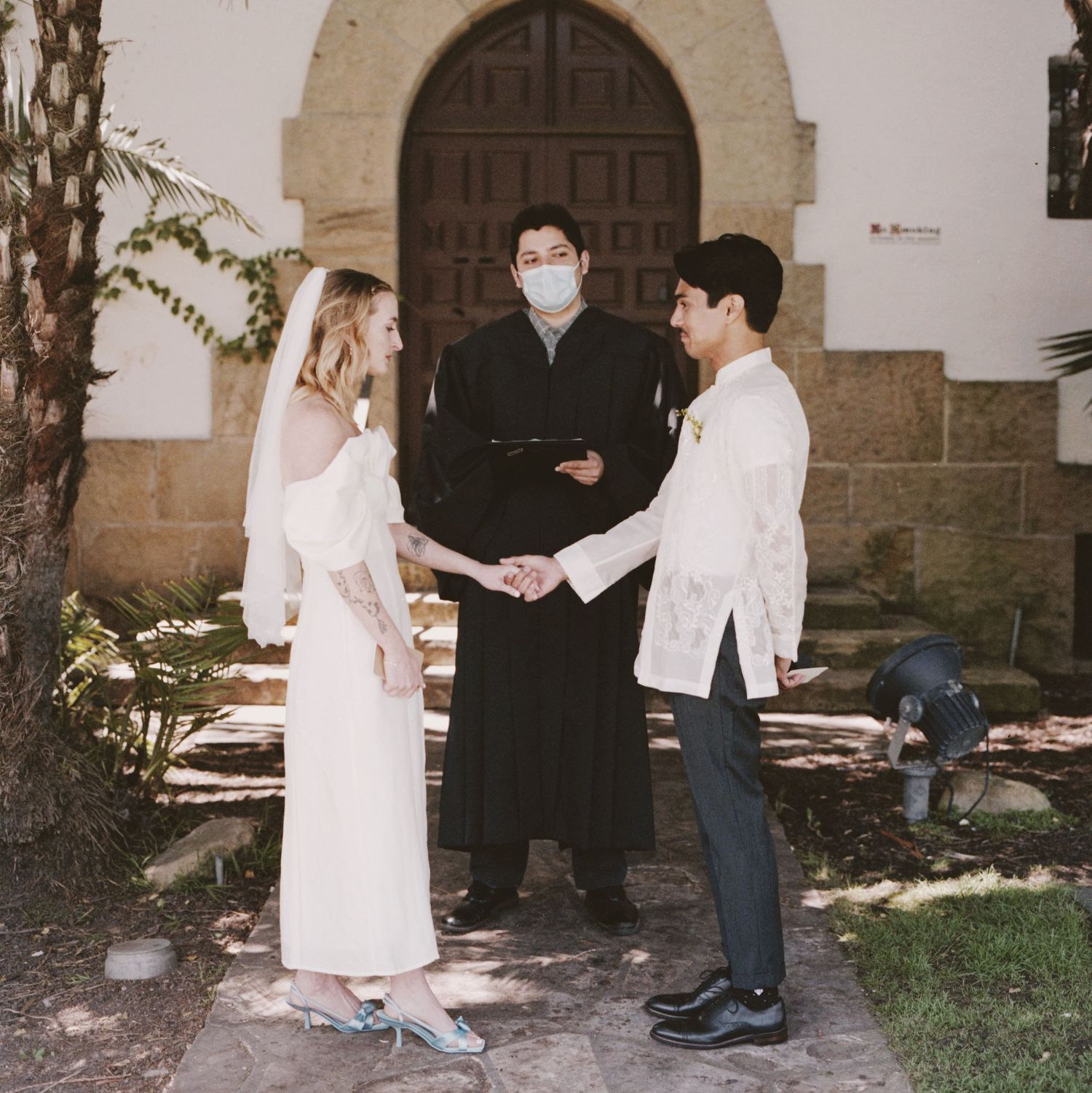 An outdoor wedding ceremony takes place in front of a historic Spanish colonial church entrance.