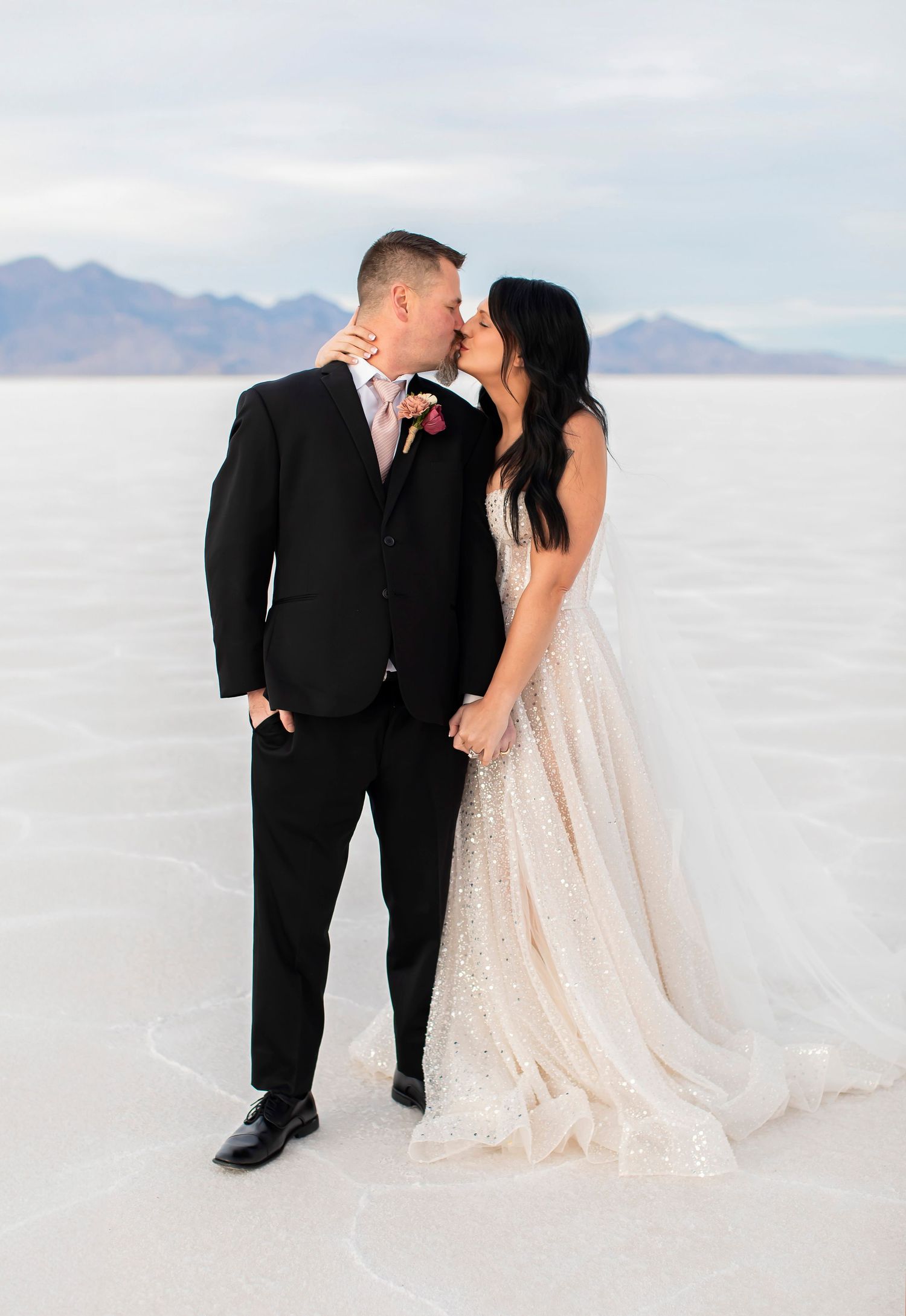 Elegant couple in formal attire sharing intimate moment on white salt flats.
