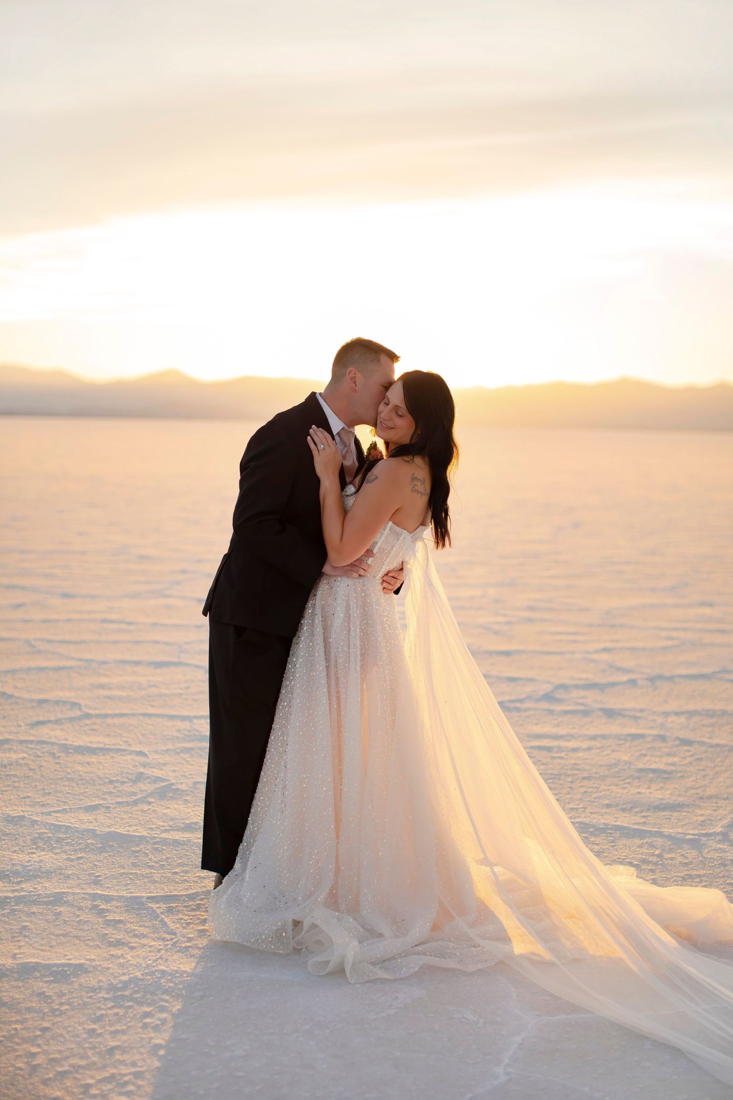 Wedding couple embraces on salt flats during sunset with flowing white dress.