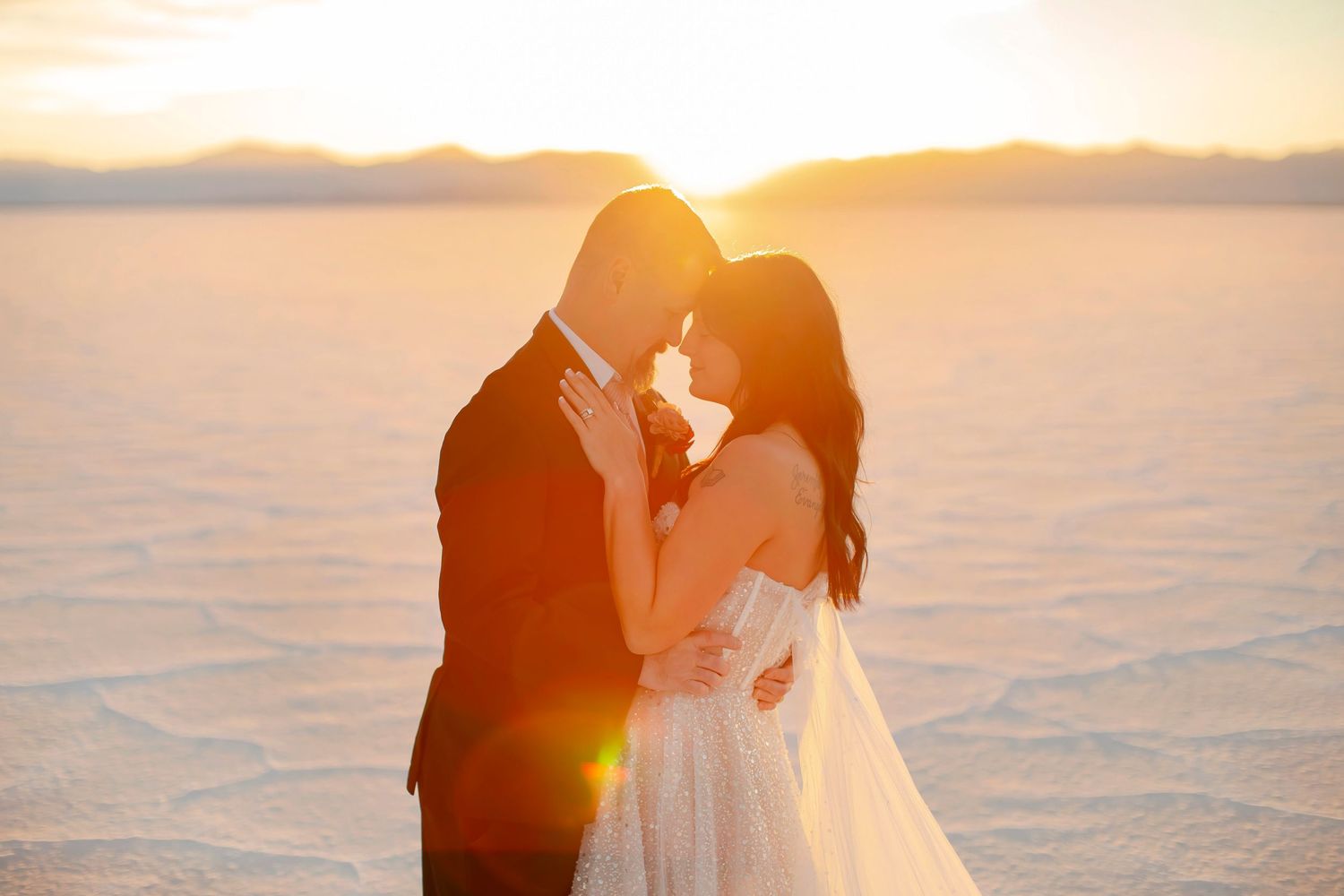 Romantic sunset portrait of newlyweds embracing on salt flats.