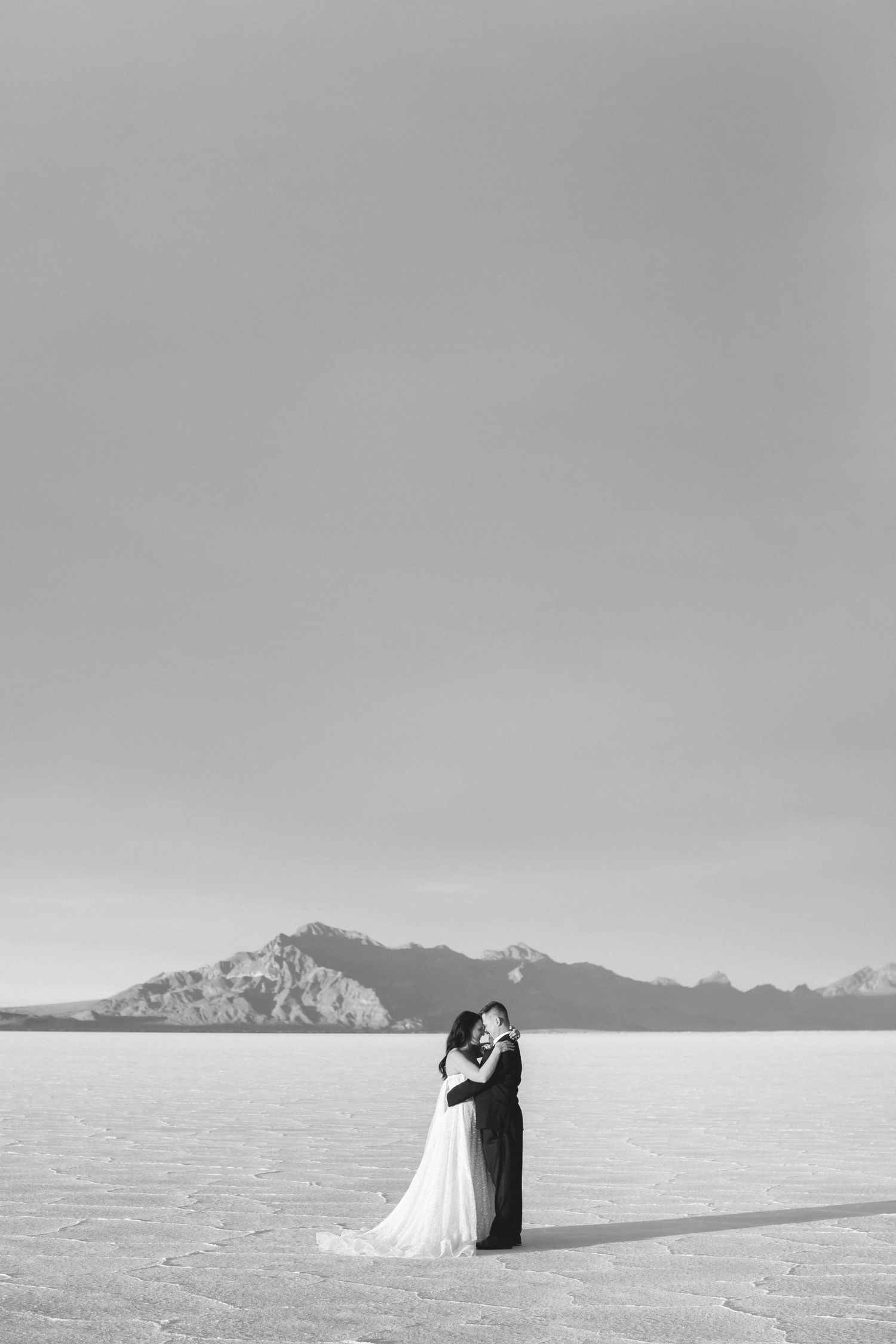 Black and white wedding portrait on salt flats with dramatic mountain landscape.