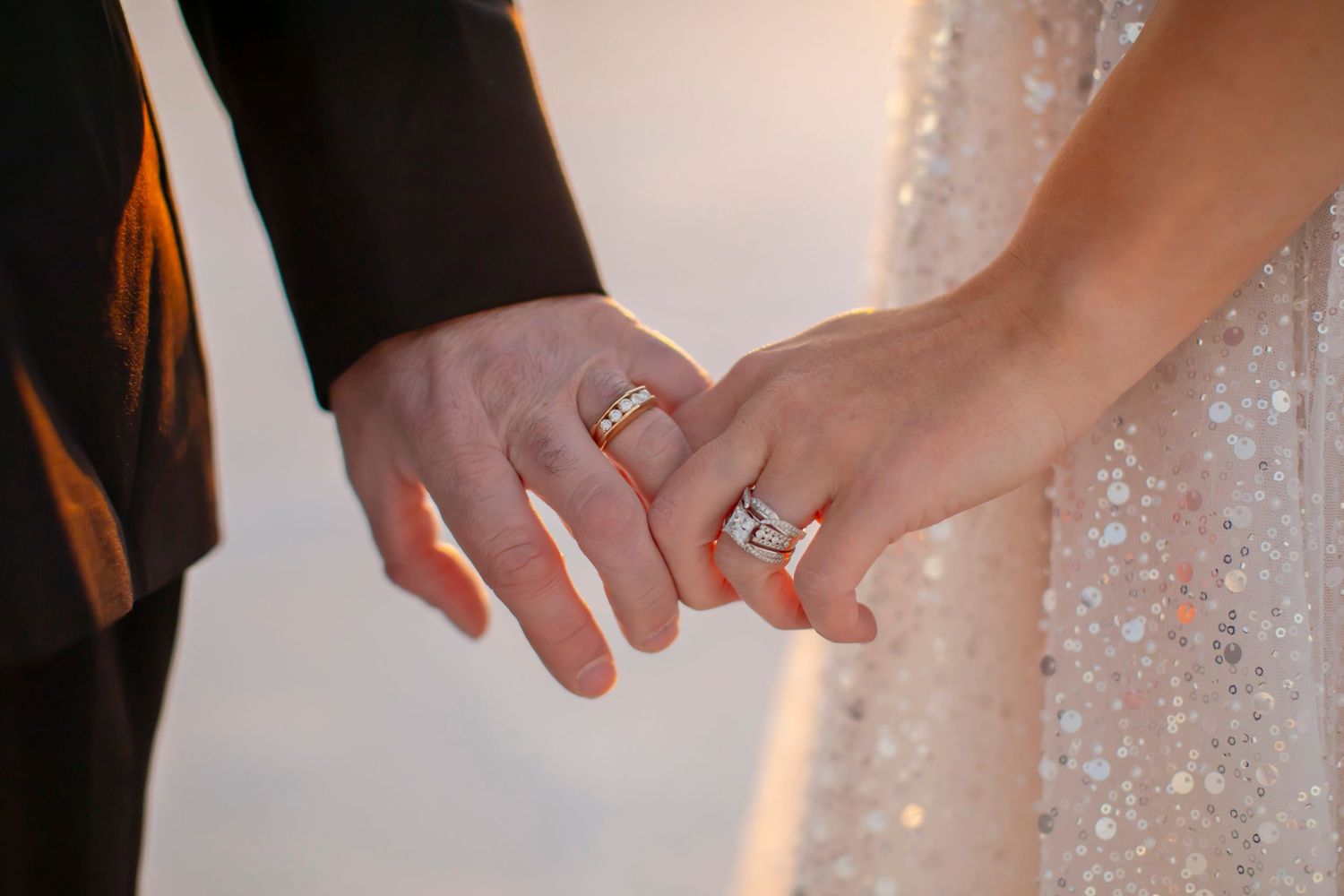 Close up of newlywed couple's hands showing wedding rings in golden light.
