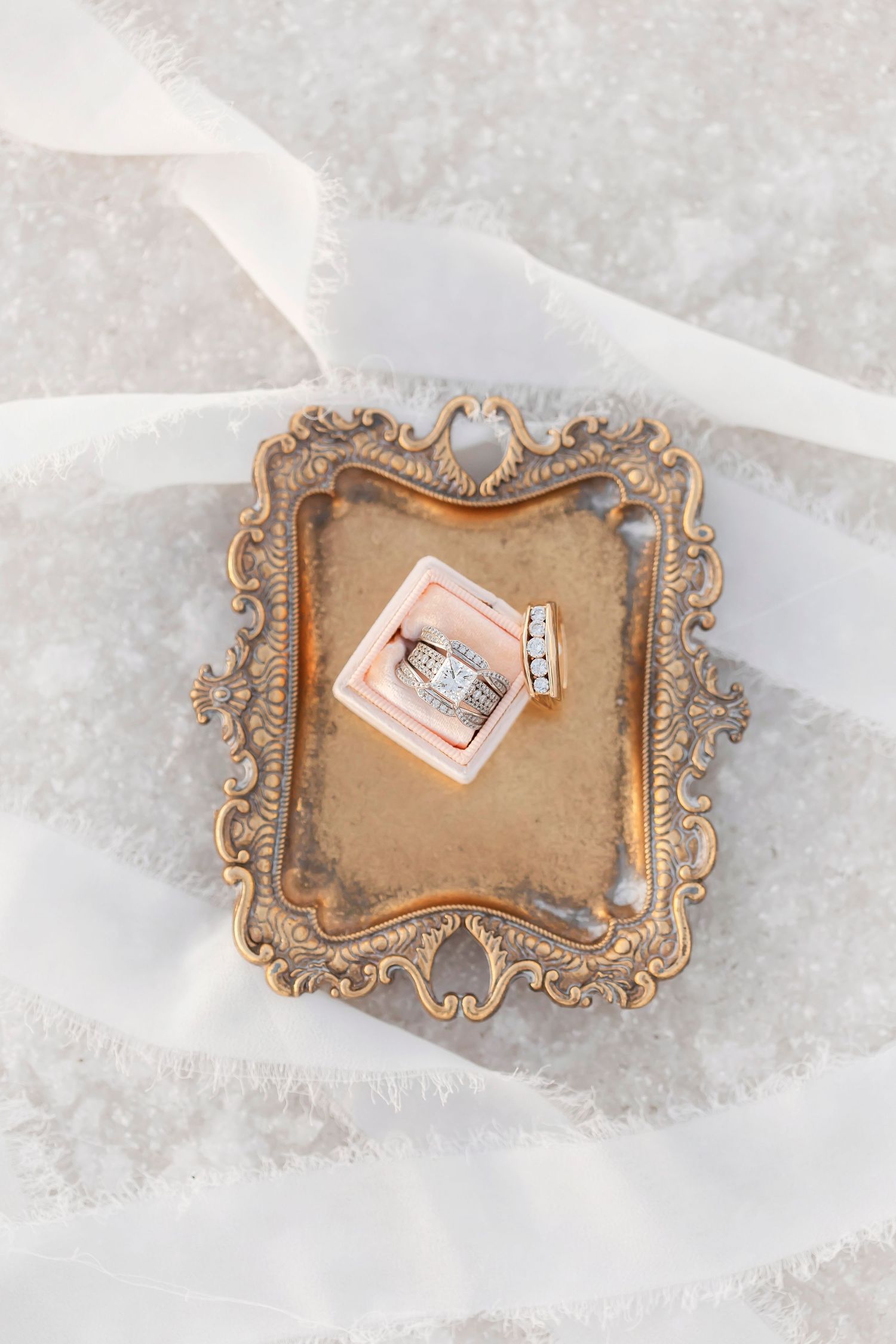 Vintage ornate gold frame displaying an engagement ring on white fabric background.