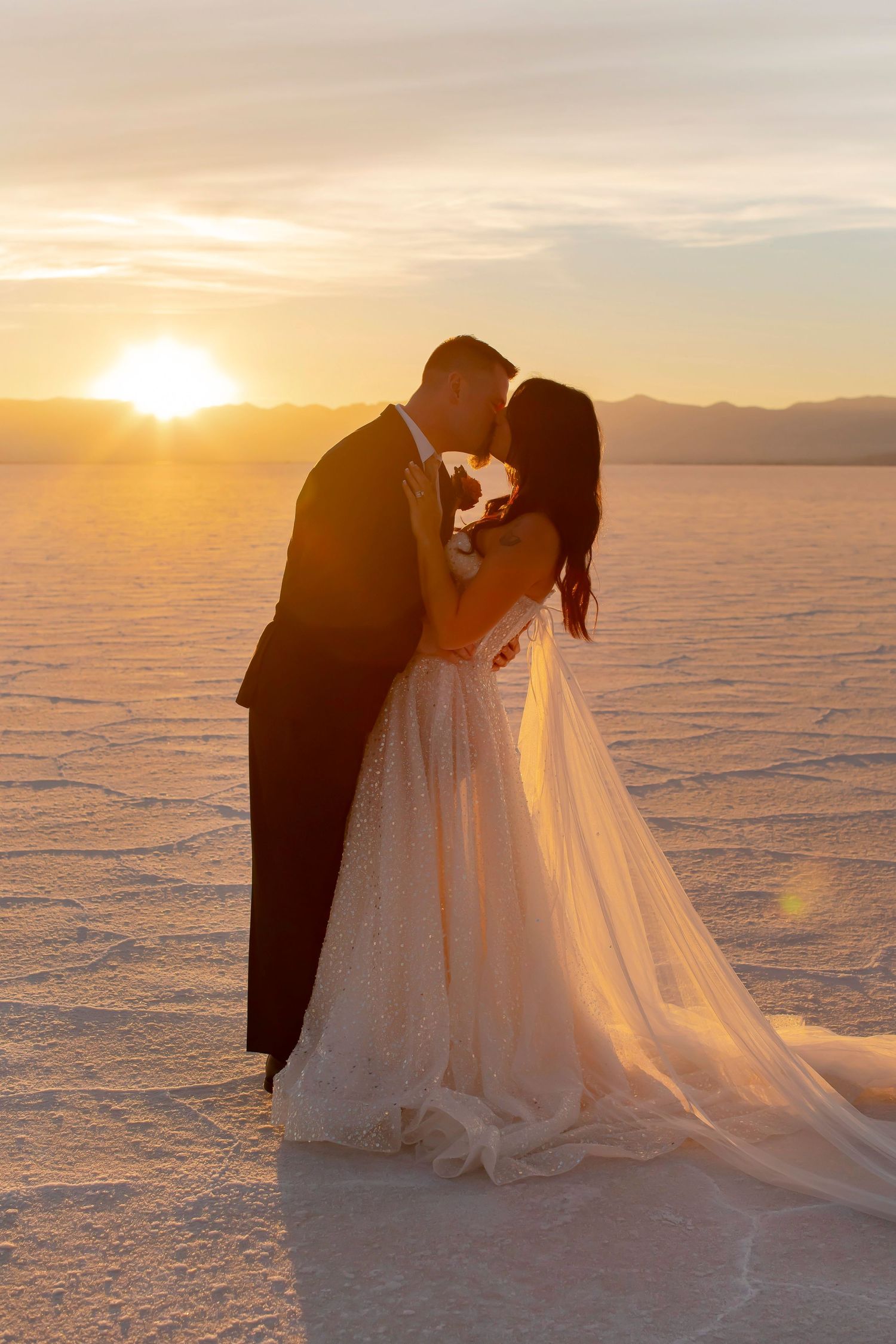 Romantic sunset silhouette of wedding couple on salt flats with golden sunburst.