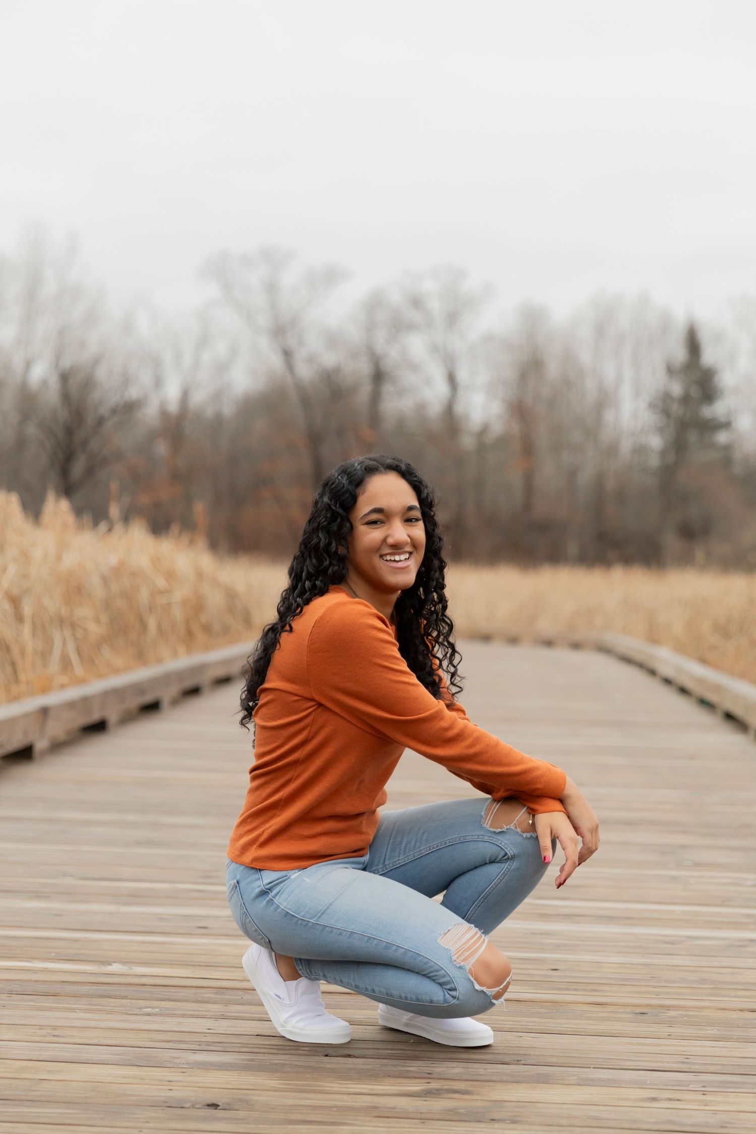 teenage girl kneeling for a photos on a wooden boardwalk in metro detroit