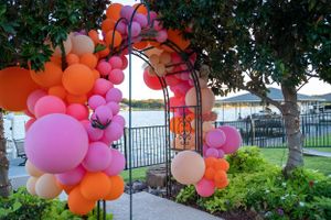 Colorful pink and orange balloon arch decorations adorning an outdoor garden pathway.