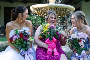 Wedding party members pose together in a cheerful outdoor setting wearing sparkly dresses.
