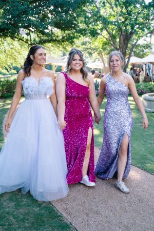 Wedding party walks together on garden path wearing white, magenta, and purple sequined dresses.