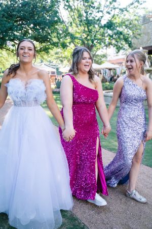 Bridesmaids laugh together while walking outdoors in coordinated sparkly formal dresses.