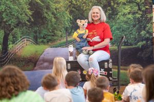 Outdoor children's performance or story time with audience seated on grass.