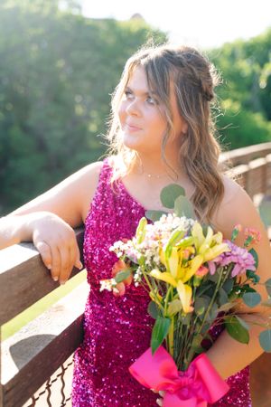 Woman in sparkly magenta dress holding colorful floral bouquet outdoors.