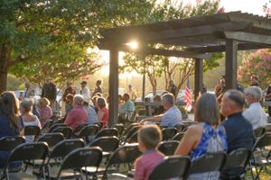 Outdoor wedding ceremony setup with rows of chairs under trees at sunset.