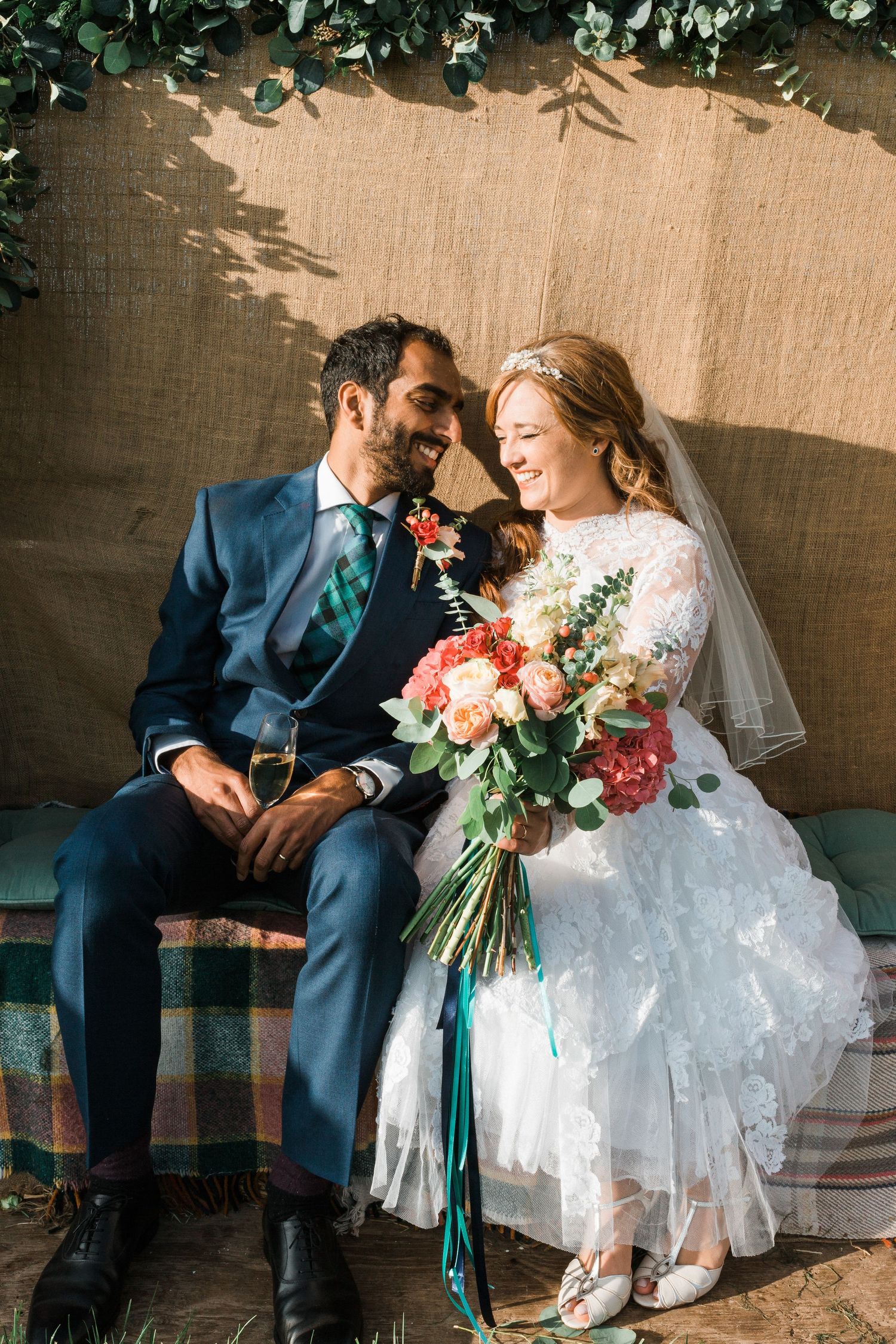 Bride & Groom sitting in the sunshine on the back of a tractor. The bride is wearing a vintage wedding dress from the 50s