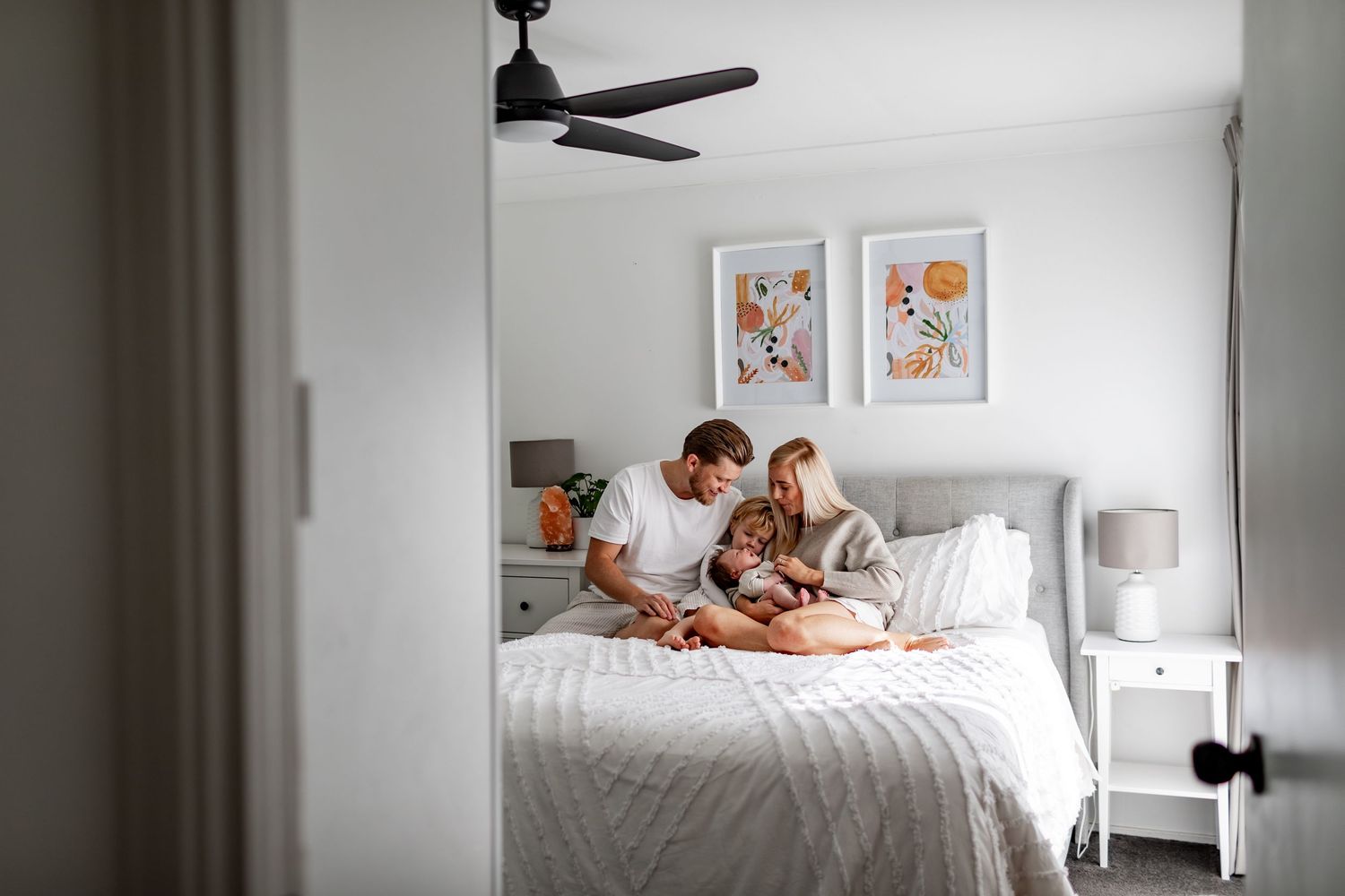 Family spending time together reading on a cozy white bed with decorative wall art.