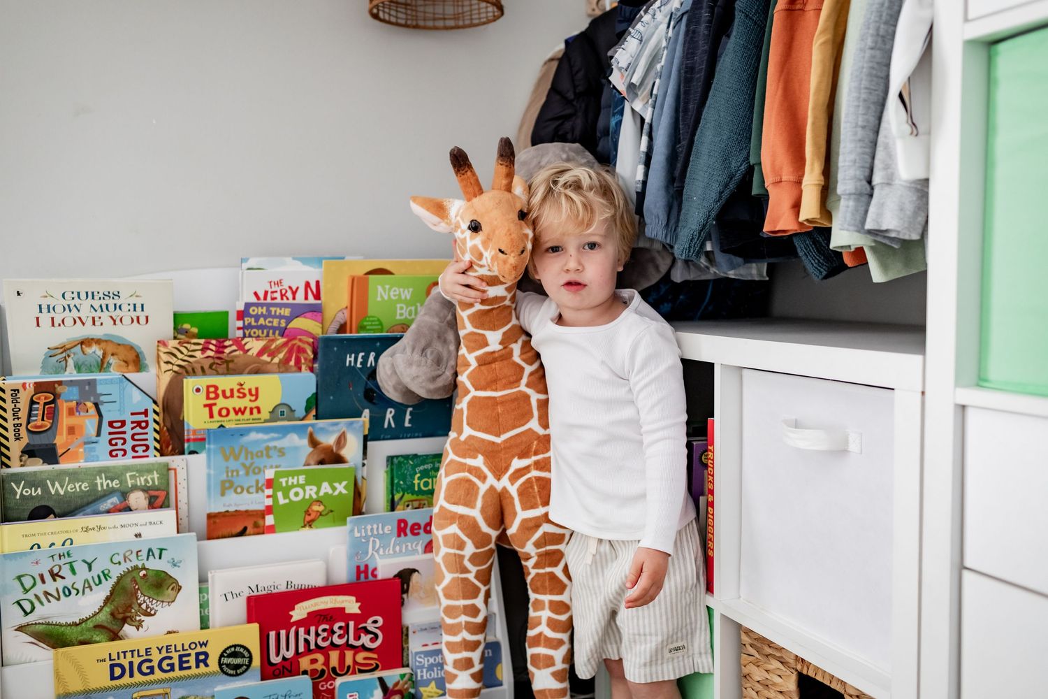 Child's room with book display, stuffed giraffe, and clothing storage.