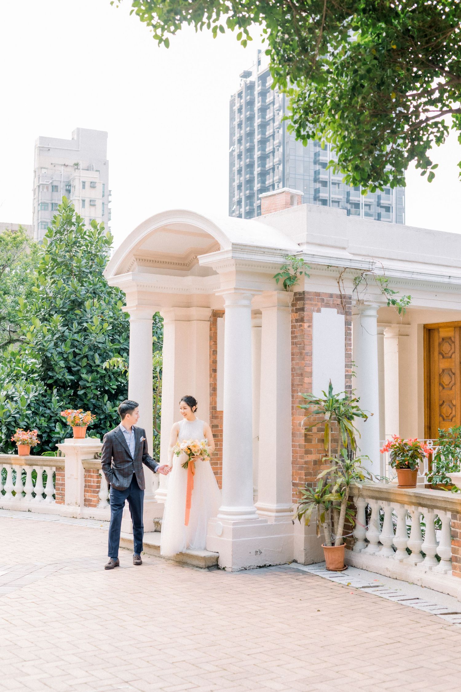 Elegant wedding couple posing at classical colonnade entrance with urban backdrop.