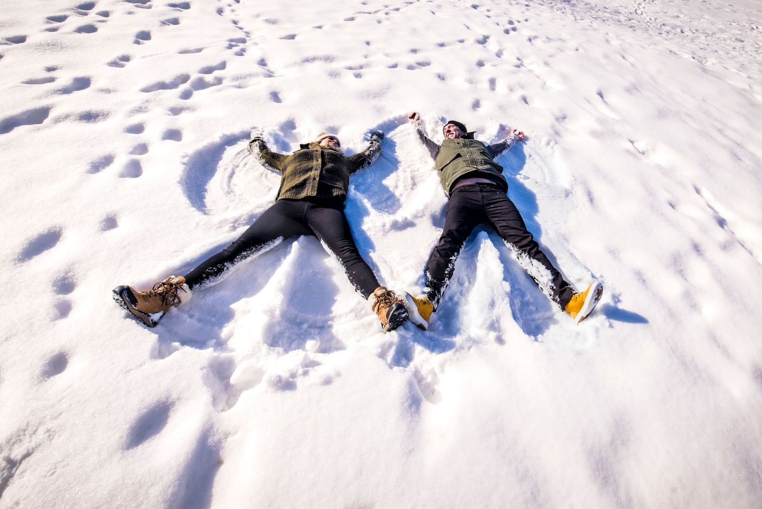 People making snow angels in fresh white snow creating symmetrical patterns.