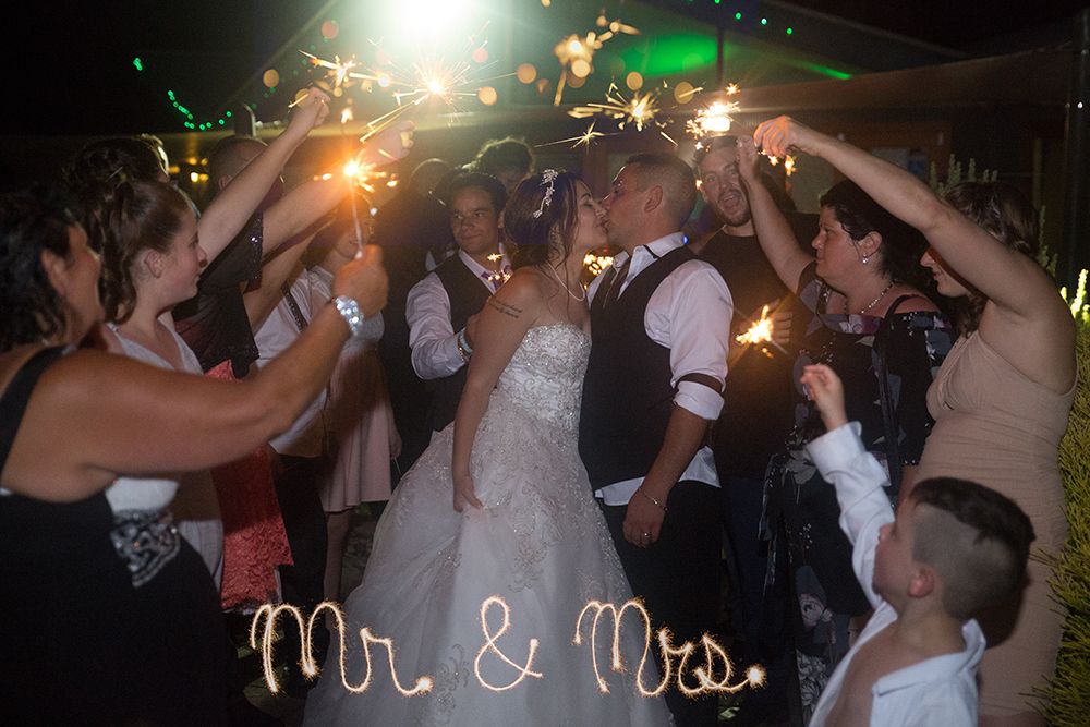 Wedding guests dancing and celebrating on a dimly lit dance floor with festive lights and decor.