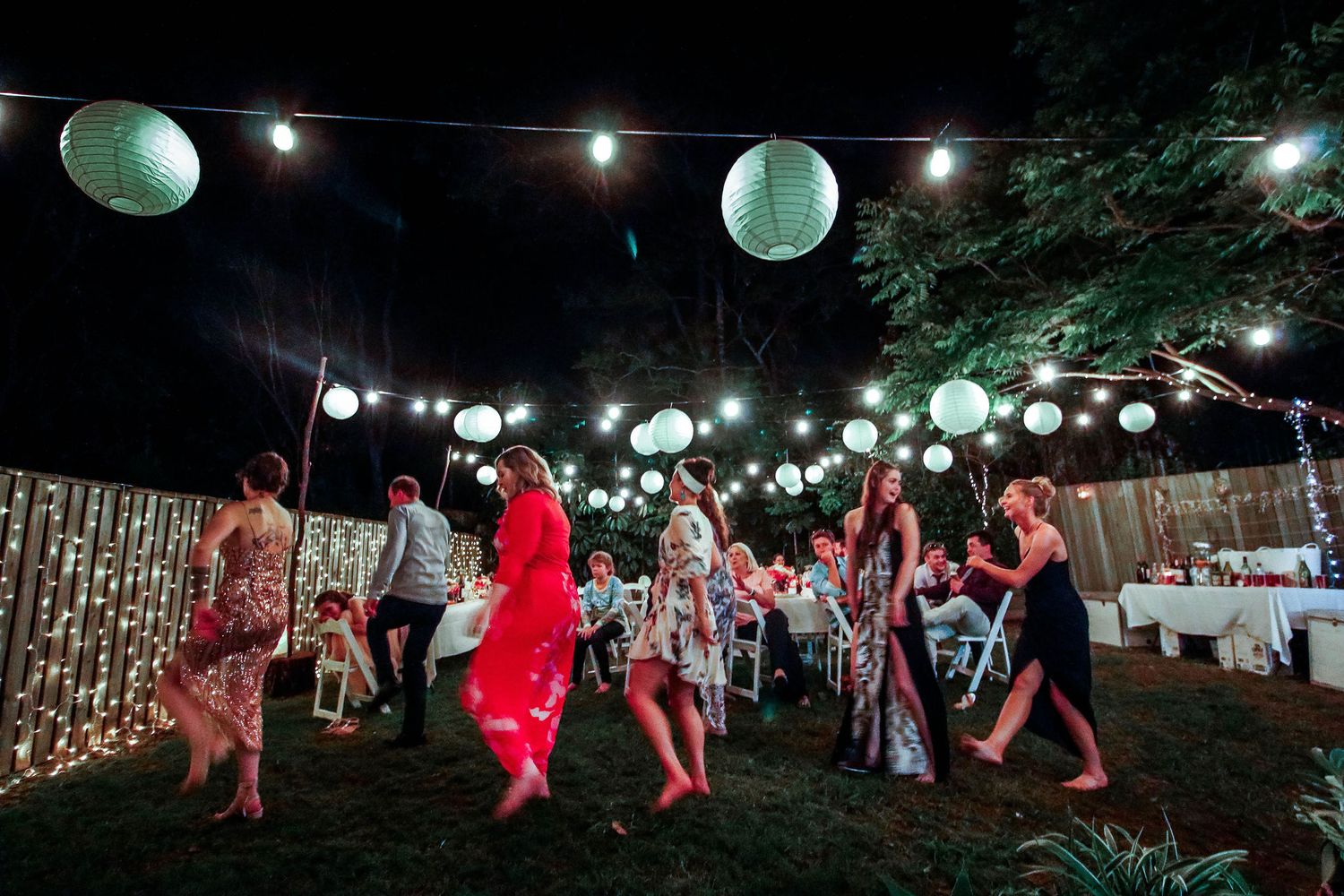 Outdoor wedding reception with glowing paper lanterns and dancing guests at night.