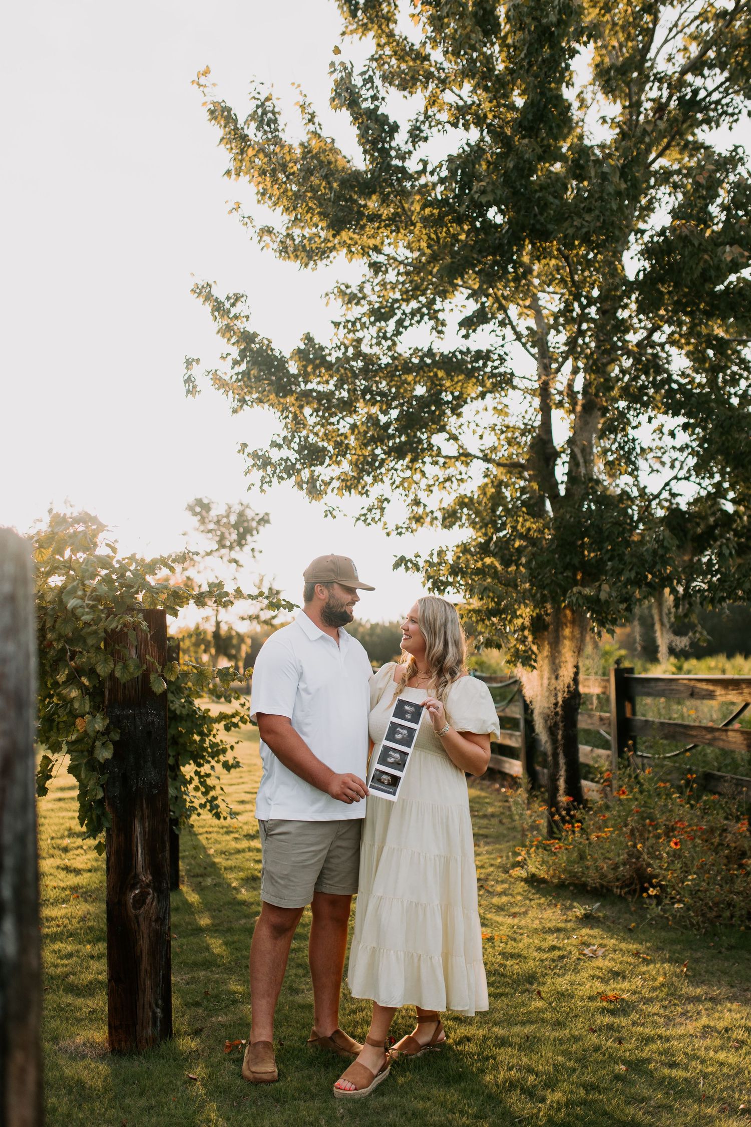 Couple holding ultrasound strip photos in golden sunset light outdoors.