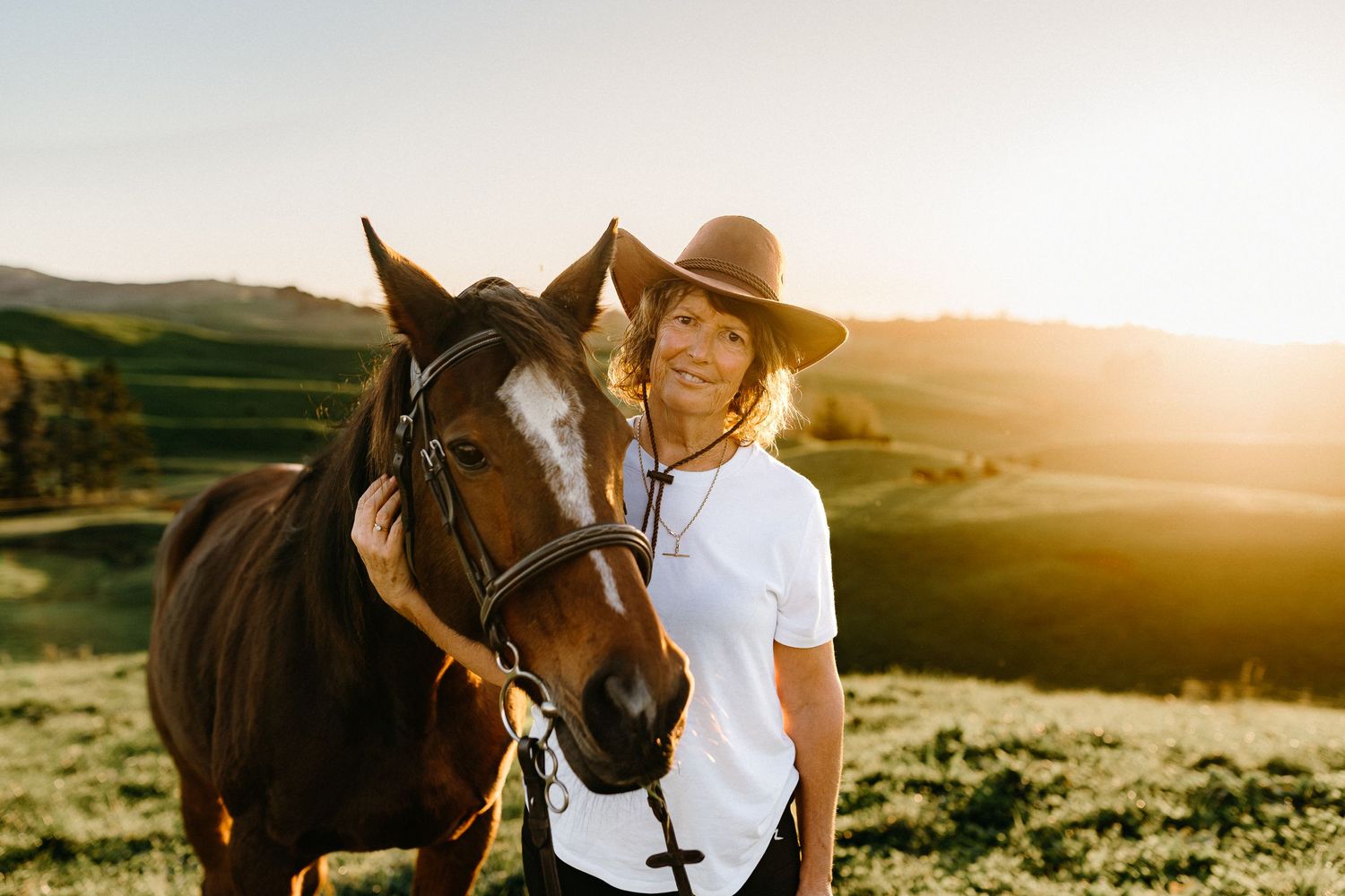 Horse and rider bonding during golden sunset in rolling countryside landscape.