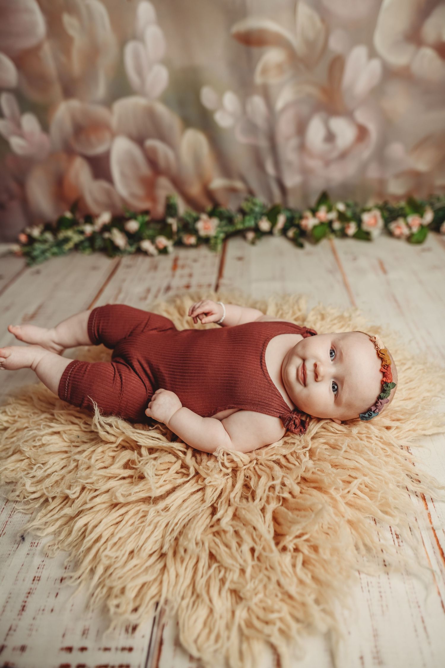 Baby in burgundy outfit lying on cream-colored textured blanket with floral accents.