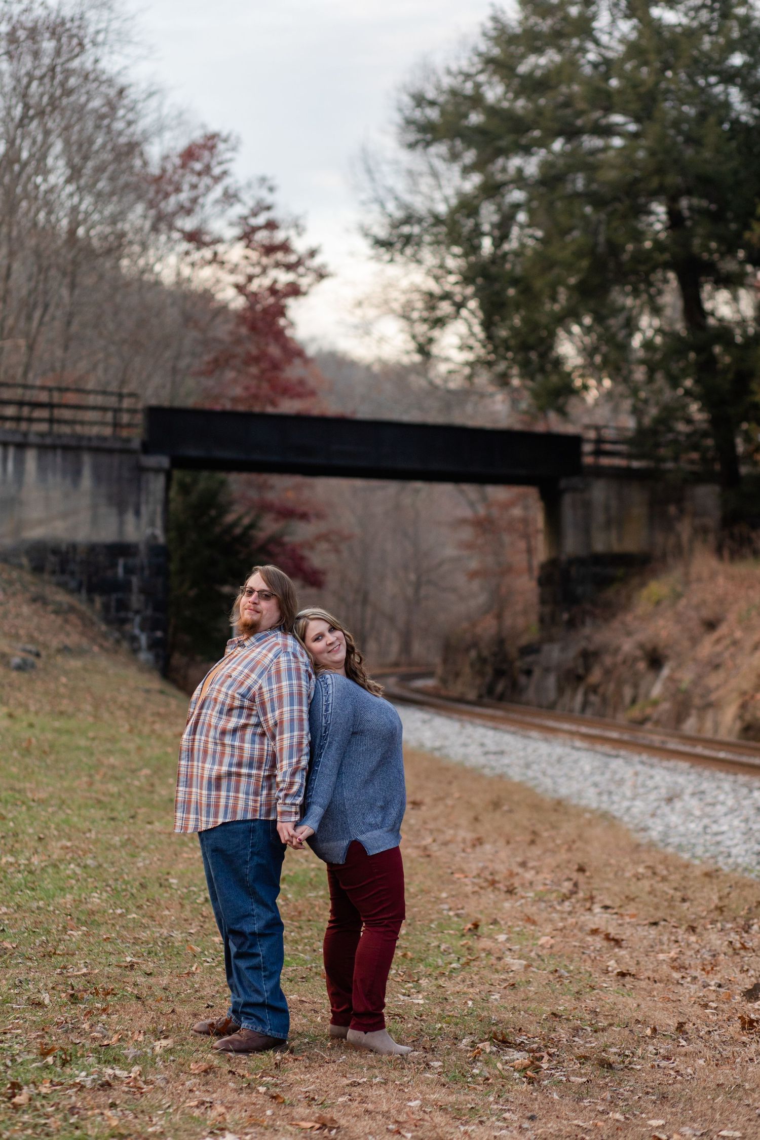 A couple walks along railroad tracks surrounded by autumn foliage and trees.