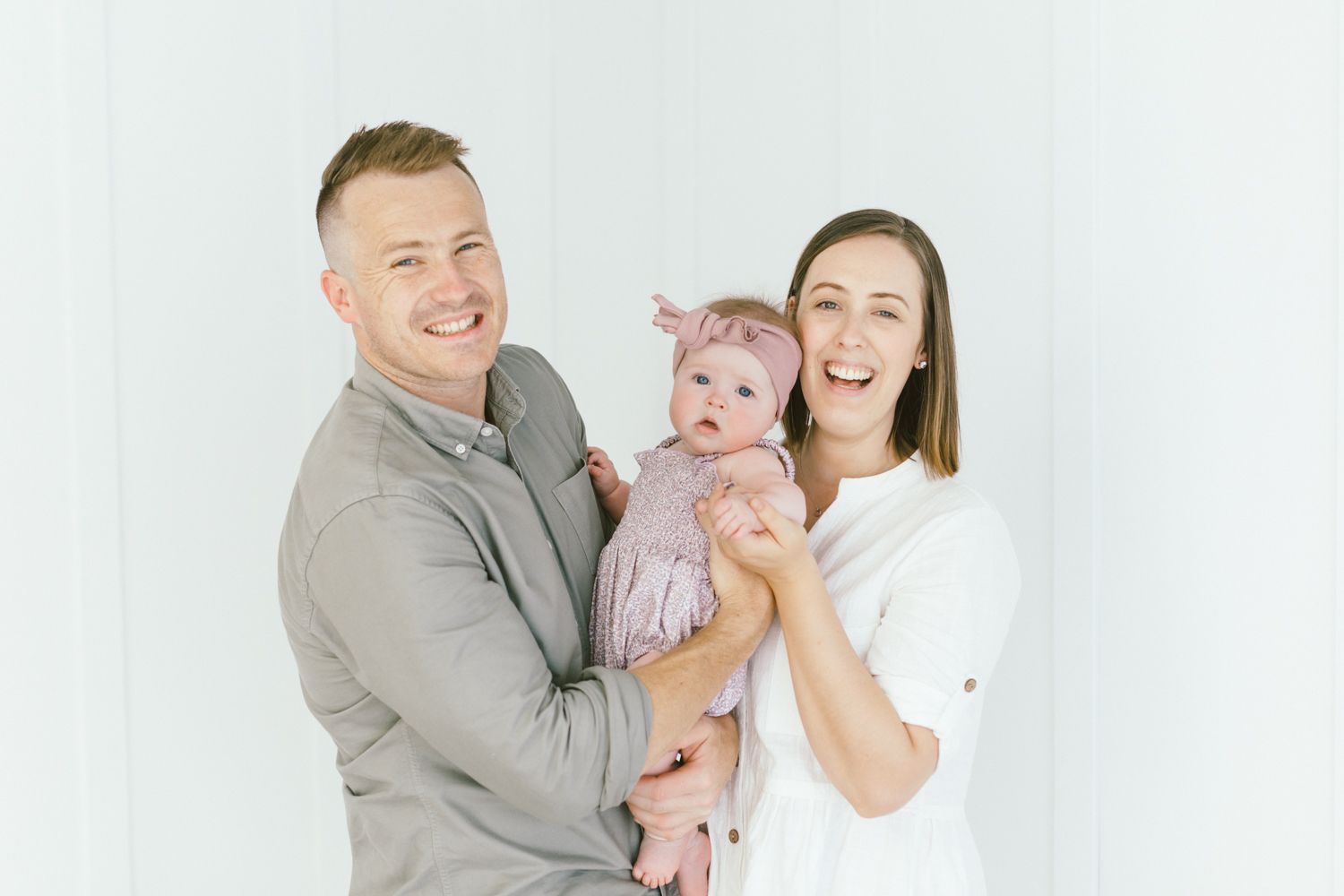 Modern family portrait against white background with baby in pink dress.