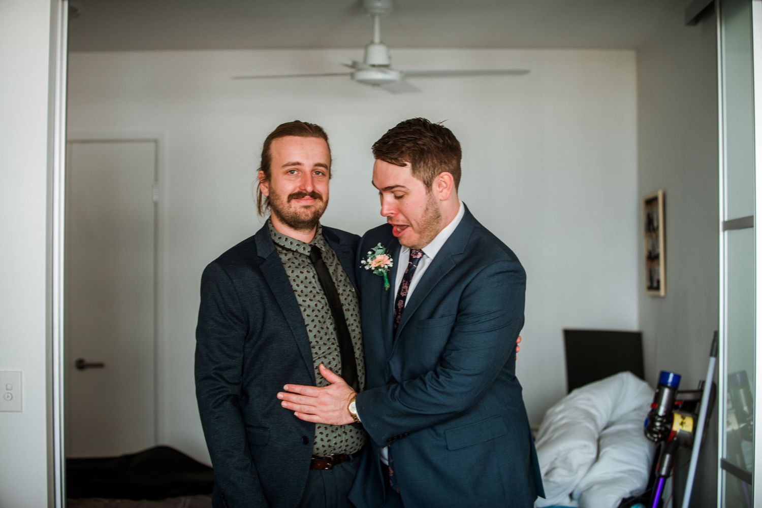 Two men in suits share a candid moment in a bright room.