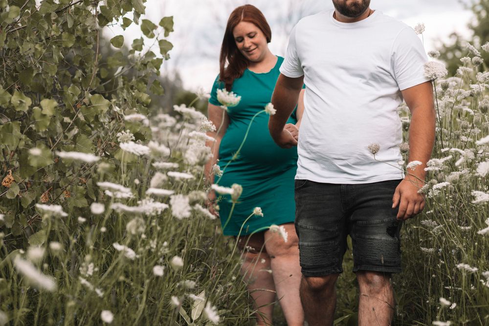 Couple standing among wildflowers during outdoor maternity photo session.