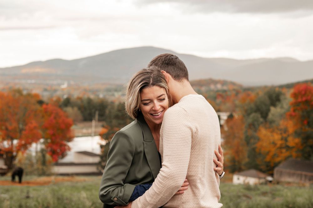 Romantic autumn scene of a couple embracing on a hillside with fall foliage in the background.