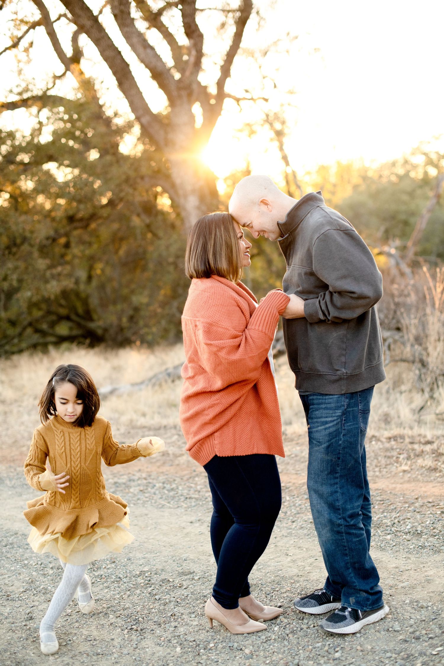 Family shares joyful moment on nature trail as child dances in yellow dress.