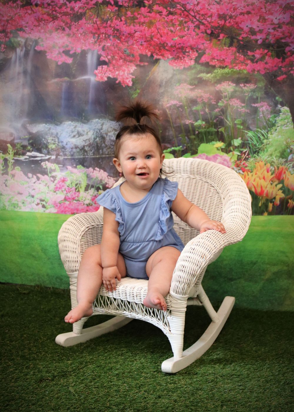 White wicker rocking chair against floral backdrop with pink cherry blossoms and waterfall scenery.