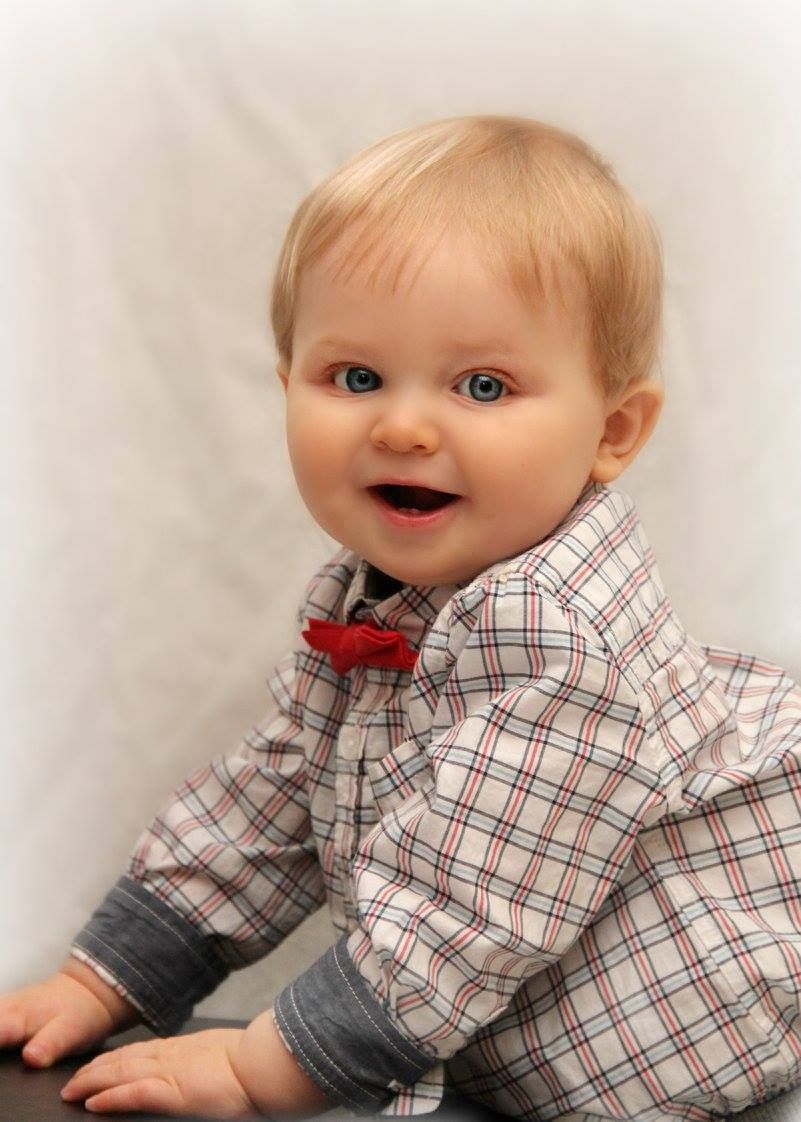Baby wearing plaid shirt and bow tie smiles during portrait session.