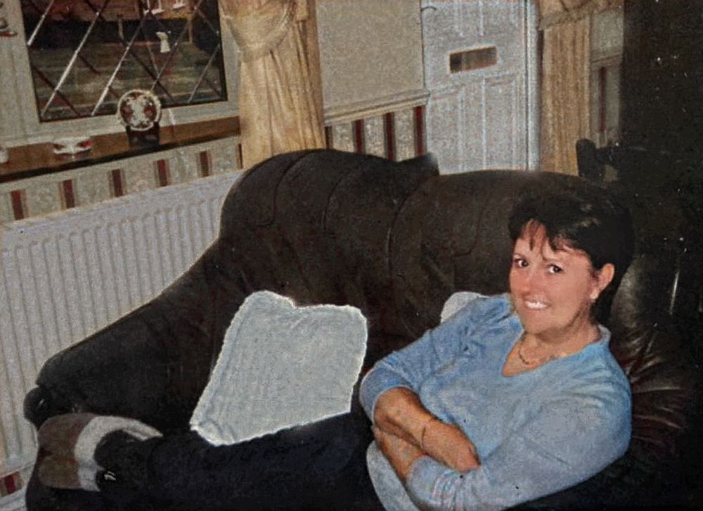 Person relaxes on brown leather couch in home setting with window visible.