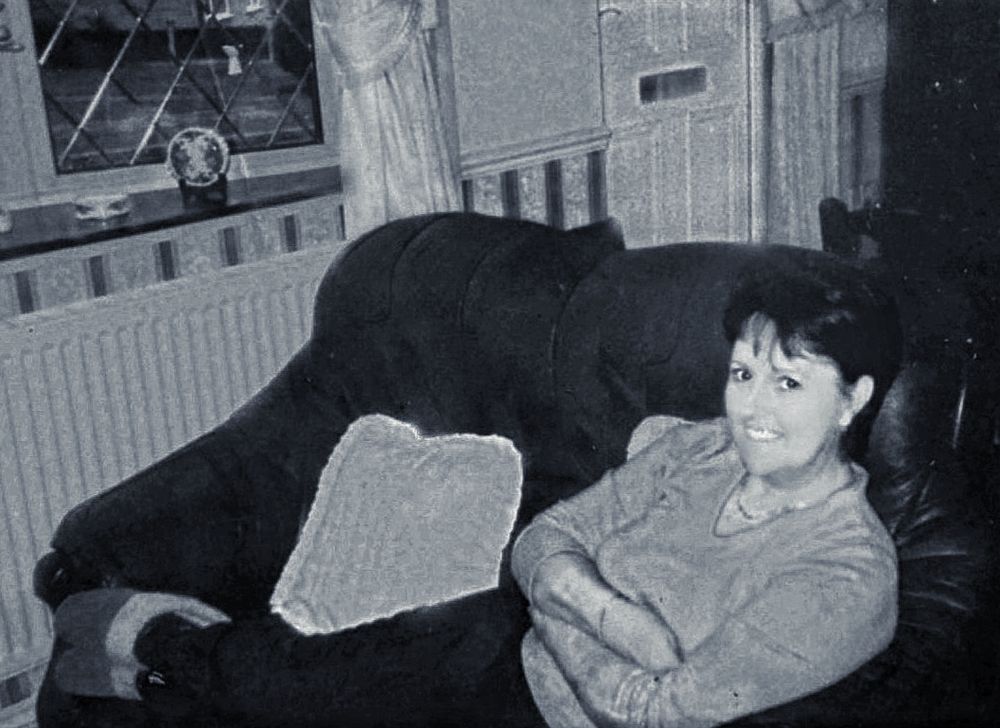 Black and white photo shows someone relaxing on dark couch in home interior.
