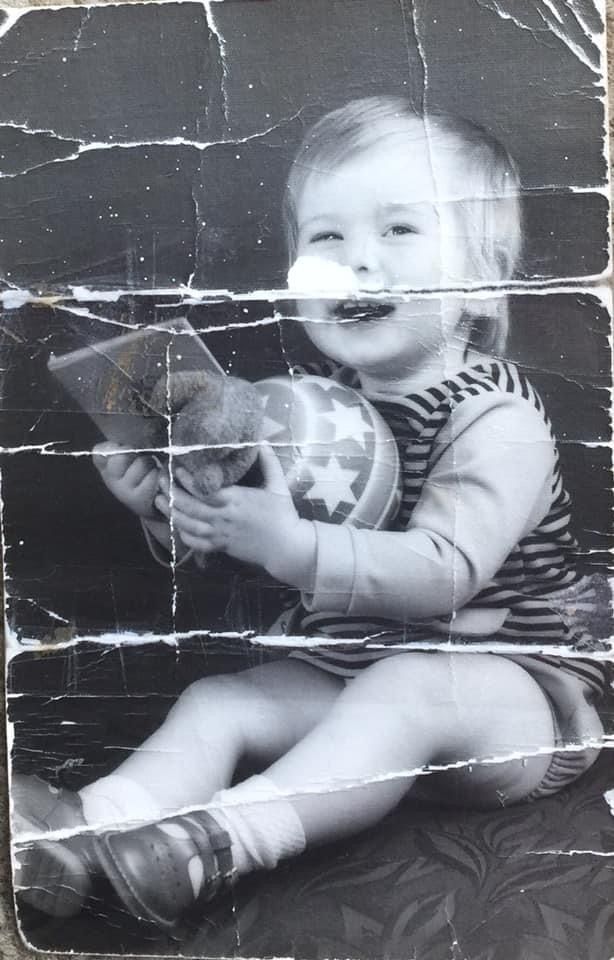 A damaged black and white photograph shows a child with a toy sitting on the ground.