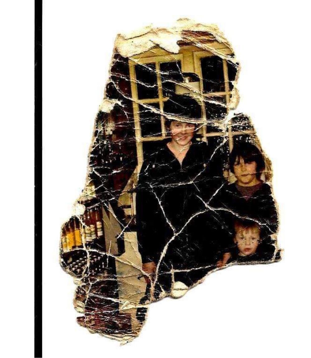 A heavily damaged vintage photograph showing three people standing together near a window.