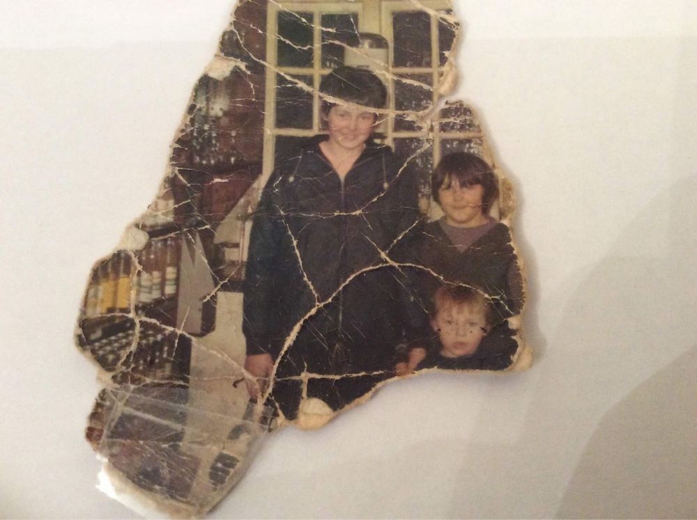 A damaged vintage family photograph with visible tears and creases.